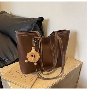 Detailed close-up of dark brown tote bag with white contrast stitching and plush charm