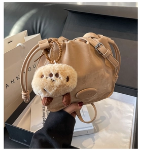 Detailed close-up of beige drawstring bucket bag with plush charm and adjustable strap