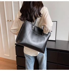 Detail showing back view of large black tote bag with white contrast stitching and gold hardware