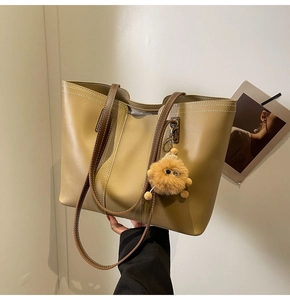 Detail of olive tote bag with contrast stitching, brown handles, and furry monster charm