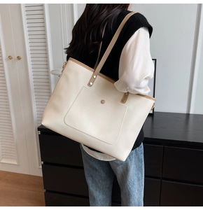 Side view of beige tote bag with khaki trim worn by model in a minimalist room