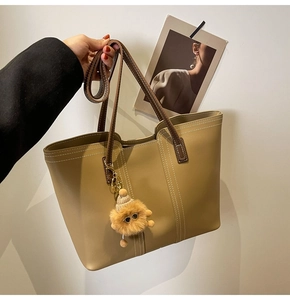 Detail of khaki tote bag with contrast stitching, brown handles and plush doll charm