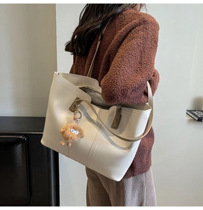 Detail of off-white tote bag with brown contrast handles and a plush mascot pendant