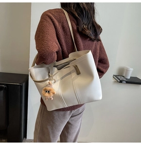 Detail view of a large cream tote bag featuring a cute brown plush charm and slim straps