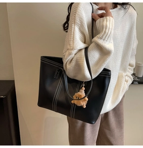 Detail of black leather tote bag with white contrast stitching and brown plush charm accessory