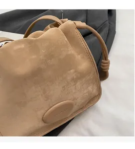 Close-up of light brown pleated crossbody bag with brushed texture and metal logo plate