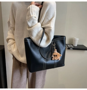 Detail of black tote bag with white contrast stitching and brown plush charm