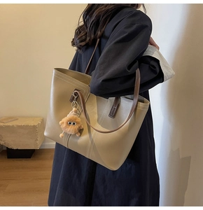 Detail of a large brown tote bag with white contrast stitching and a lion plush pendant