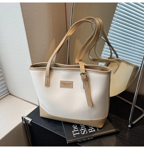 Détail d'un sac cabas en cuir crème avec sangle camel sur livre sous une ombre douce