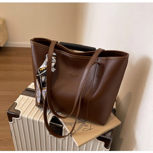 Detail of large brown leather tote bag with decorative silk scarf on a suitcase