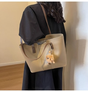 Detail of khaki leather tote bag featuring contrast white stitching and plush charm