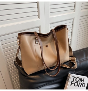 Close-up of khaki leather tote bag with brown trim and dual shoulder strap detail