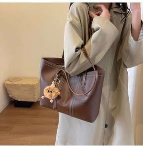Brown leather tote bag detail with white contrast stitching and plush charm on shoulder