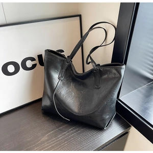 Detail view of black tote bag with pleated texture on a dark wood surface