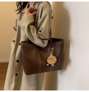 Detail of dark brown tote bag with white contrast stitching and plush eye charm on coat