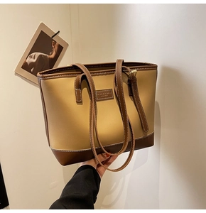 Détail du sac cabas kaki avec écusson en cuir de mode et anses marron contrastées