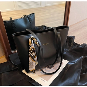 Close-up of black matte leather tote bag with silk scarf and gold lettering detail