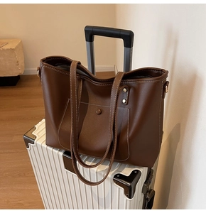 Detail of large brown leather tote bag with white stitching on a white suitcase