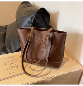 Détail d'un sac cabas en cuir marron avec surpiqûres blanches et logo embossé