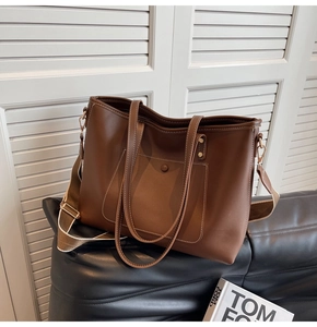 Detail of a dark brown faux leather tote bag with white stitching and wide shoulder strap
