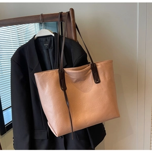 Close-up of beige tote bag with pleated texture and long brown leather handles hanging