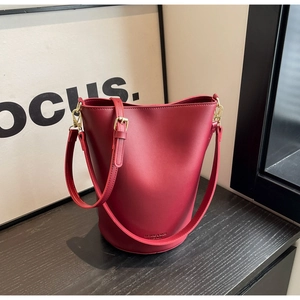 Macro detail of dark red bucket bag featuring matte texture and gold-tone hardware