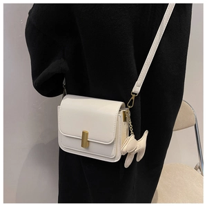 Detail of white square crossbody bag with gold metal buckle and cute dog charm pendant