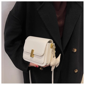 Détail d'un sac bandoulière en cuir beige avec fermoir doré et pendentif en nœud