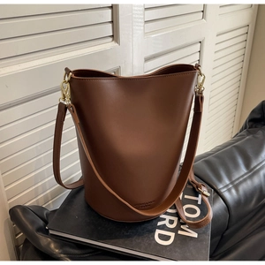 Detail of brown leather bucket bag with gold hardware on a fashion book background