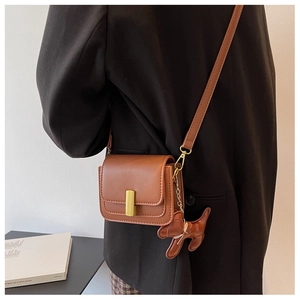 Detail of a brown leather crossbody square bag with a cute dog pendant and gold buckle