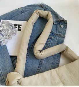 Detail of light beige pleated shoulder bag with wide padded handle on denim fabric