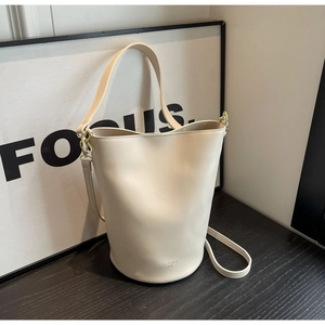 Detail of cream bucket bag with wide shoulder strap and gold hardware on wood