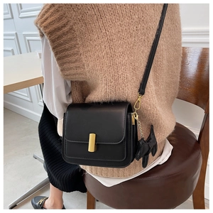 Detail of minimalist black crossbody bag with gold buckle and cute dog pendant accessory