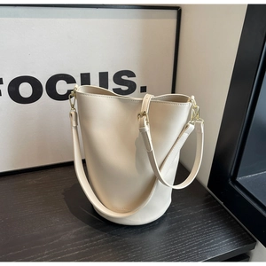 Macro detail of creamy white PU leather bucket bag with gold hardware and brand logo