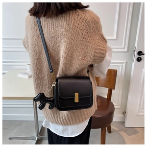 Detail of black crossbody bag with gold lock and cute dog charm on a female model