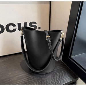 Detail of black matte bucket bag featuring gold buckles and adjustable shoulder strap