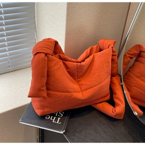 Detailed view of the bright orange quilted puffer bag with a large knot shoulder strap