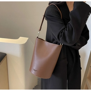 Detail of a brown leather bucket bag with adjustable strap shown on a model side view