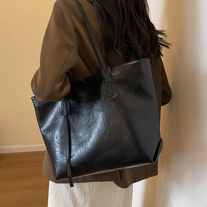 Large black tote bag with glossy pleated texture worn by a model in a minimalist setting
