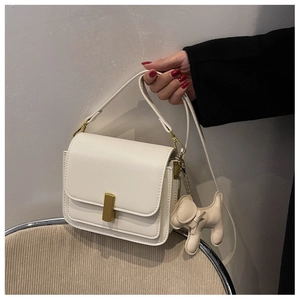 Détail d'un sac bandoulière blanc crème avec boucle dorée et charm chien sur une chaise