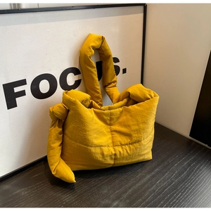 Detail of yellow quilted puffer tote bag with knotted shoulder strap on wooden surface