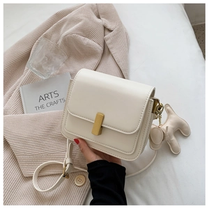 Detail of cream white faux leather flap bag with gold buckle and dog charm on cozy bedding