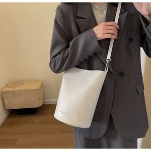 Detail of cream leather bucket bag with shoulder strap and minimalist metal hook hardware