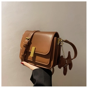 Detail of brown leather crossbody bag with gold buckle and cute puppy-shaped charm