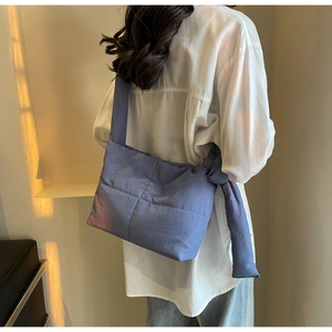 Blue quilted tote bag with unique knot detail shown on model in warm indoor lighting