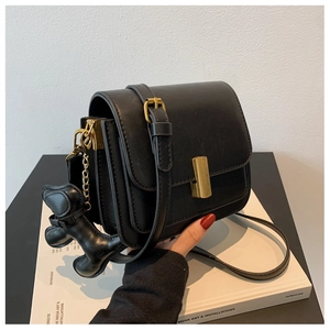 Detail of black matte leather crossbody bag with gold buckle and a small dog charm