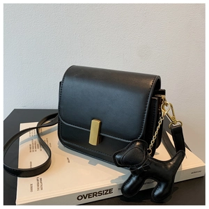 Detail of black crossbody bag with gold hardware and a cute dog charm on a white book