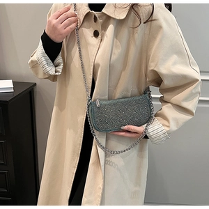 Close-up of a dark green rhinestone crossbody bag with a silver chain on a beige coat