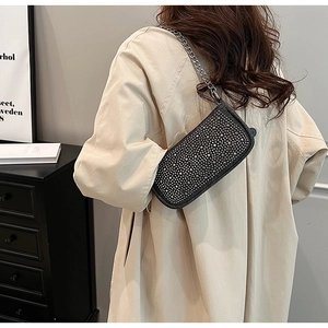 Close-up of a black rhinestone underarm bag with a silver chain on a beige coat
