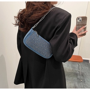 Detail of blue denim underarm bag with silver studs and metal chain on black suit
